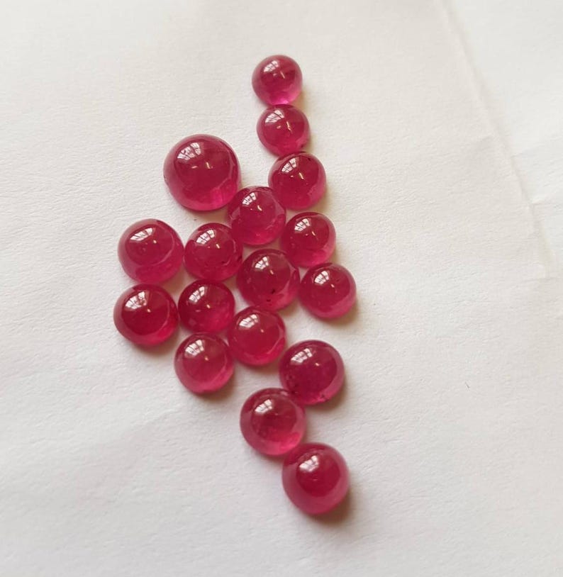 May include: A collection of 18 round, cabochon-cut ruby gemstones. The stones are various sizes and shades of red.