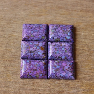 Könnte beinhalten: Sechs quadratische, violette und goldene Edelsteinkabochons. Die Cabochons sind in zwei Reihen zu je drei angeordnet.