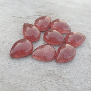 May include: Eight teardrop-shaped, translucent pink gemstone cabochons with a sparkly, speckled texture.