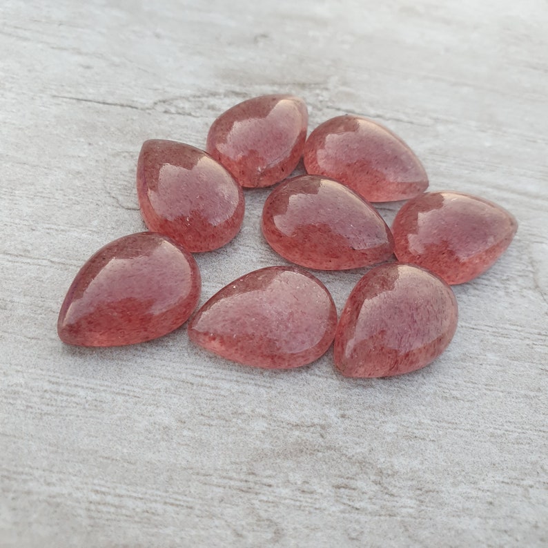 May include: Eight teardrop-shaped, translucent pink gemstone cabochons with a sparkly, speckled texture.