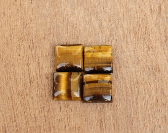 May include: Four square-shaped tiger's eye gemstones on a wooden surface. The gemstones are a mix of brown and gold.