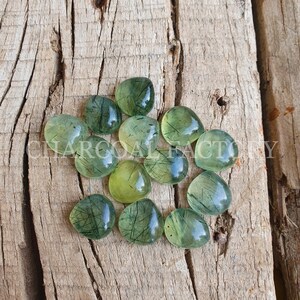 May include: A collection of 10 green aventurine cabochons with black inclusions. The cabochons are heart-shaped and have a smooth, polished finish.
