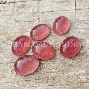 May include: Six oval-shaped, translucent, pink gemstones with a speckled, red-brown pattern.