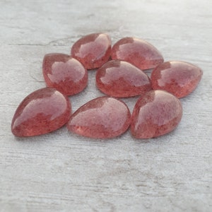 May include: Eight teardrop-shaped, translucent pink quartz stones with a speckled, cloudy appearance.