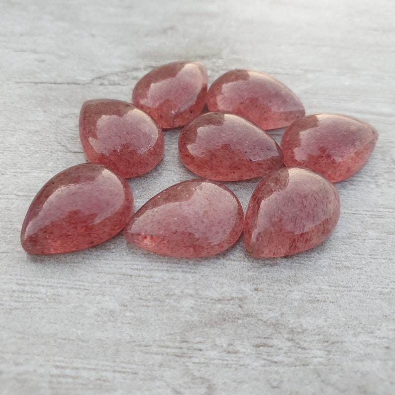 May include: Eight teardrop-shaped, translucent pink quartz stones with a speckled, cloudy appearance.