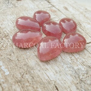 May include: Seven pink teardrop-shaped glass cabochons with a sparkly, translucent finish.