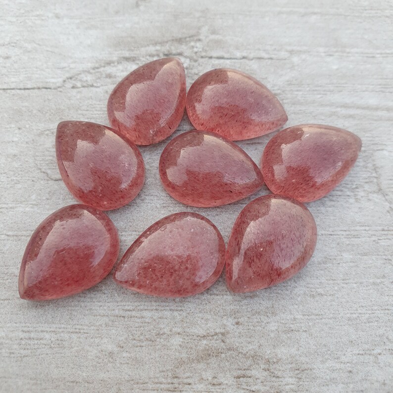 May include: Eight teardrop-shaped, translucent pink quartz cabochons with a sparkly, speckled texture.