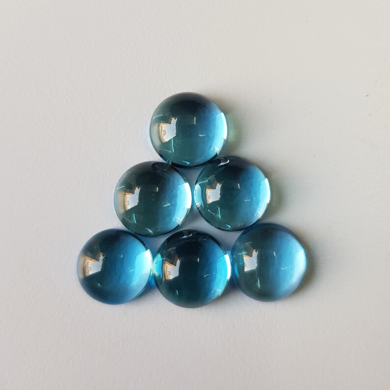 Op de afbeelding: Zes ronde, blauwe glazen cabochons gerangschikt in een driehoekig patroon.