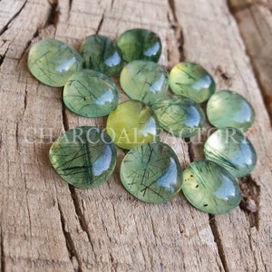 May include: A collection of green and yellow gemstone cabochons with a translucent, cloudy appearance. The stones have a unique, natural pattern of black inclusions that resemble thin lines or threads.