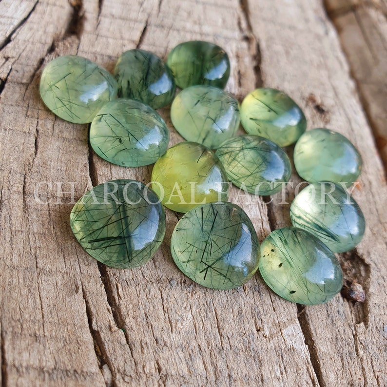 May include: A collection of green and yellow gemstone cabochons with a translucent, cloudy appearance. The stones have a unique, natural pattern of black inclusions that resemble thin lines or threads.