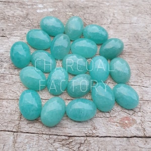 Puede incluir: Una colección de 16 piedras preciosas ovaladas de color verde azulado claro. Las piedras son lisas y pulidas, con un ligero brillo.