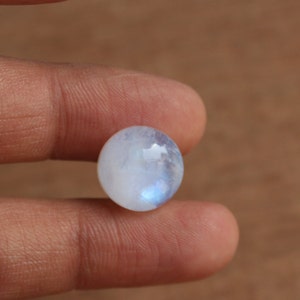 May include: A round, white moonstone cabochon with a blue iridescent sheen.