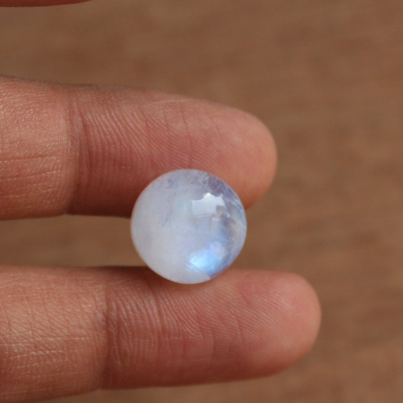 May include: A round, white moonstone cabochon with a blue iridescent sheen.