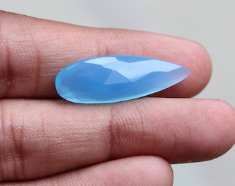 May include: A light blue gemstone with a faceted, teardrop shape. The gemstone is held in a hand.