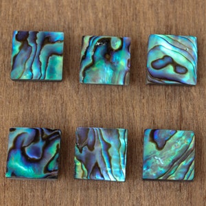 May include: Six iridescent blue and green abalone shell tiles with a smooth, polished surface.