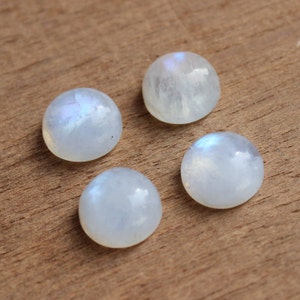 May include: Four round, white moonstone cabochons with iridescent blue and white flashes. The stones are smooth and polished.