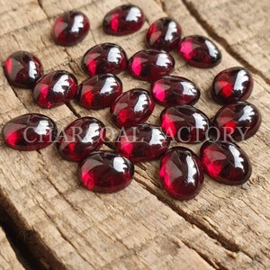 May include: A collection of 20 oval-shaped, deep red gemstones. The gemstones are smooth and polished, with a glossy finish.