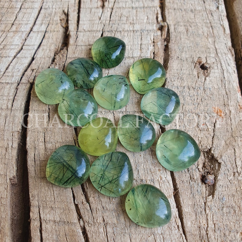 May include: A collection of green and yellow gemstone cabochons with a unique, striated pattern. The cabochons are heart-shaped and have a translucent appearance.