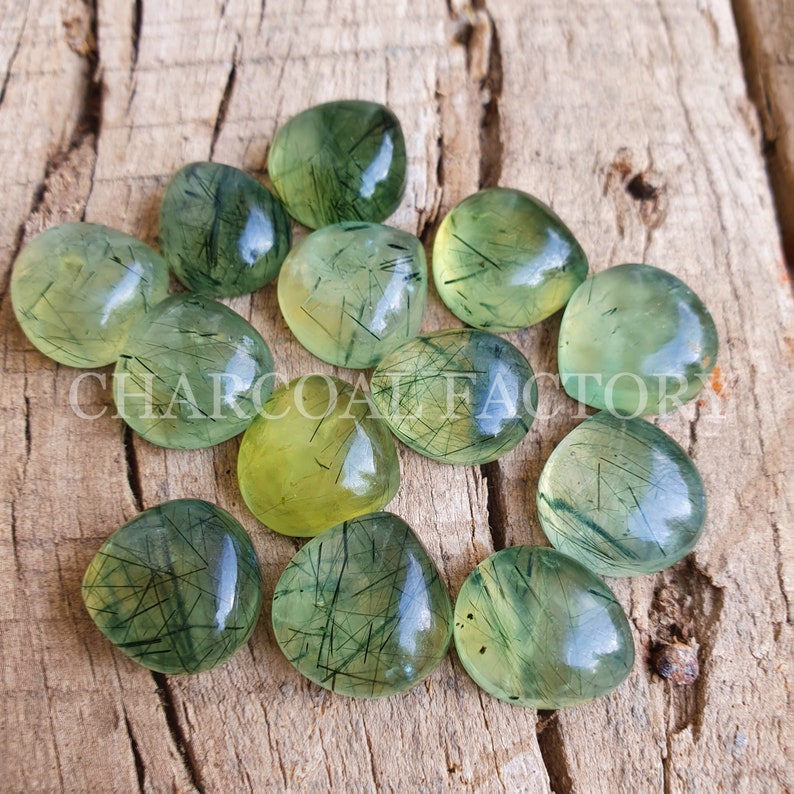 May include: A collection of 12 green and yellow gemstone cabochons with a unique, striated pattern. The cabochons are heart-shaped and have a smooth, polished finish.