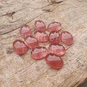 Peut inclure: Un groupe de 10 pierres ovales translucides roses avec une texture scintillante et brillante. Les pierres sont éparpillées sur une surface en bois.