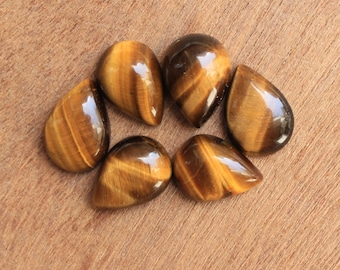 May include: Six teardrop-shaped tiger's eye gemstones in shades of brown and gold. The stones are arranged in a circle on a wooden surface.