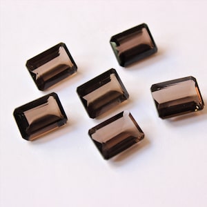 May include: Six smoky quartz gemstones in a rectangular emerald cut. The gemstones are a dark brown colour and have a smooth, polished finish.