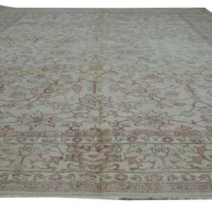 May include: A large, rectangular rug with an intricate floral pattern in shades of beige and faded rose. The rug features a detailed border and a distressed, vintage appearance, suitable for home decor.
