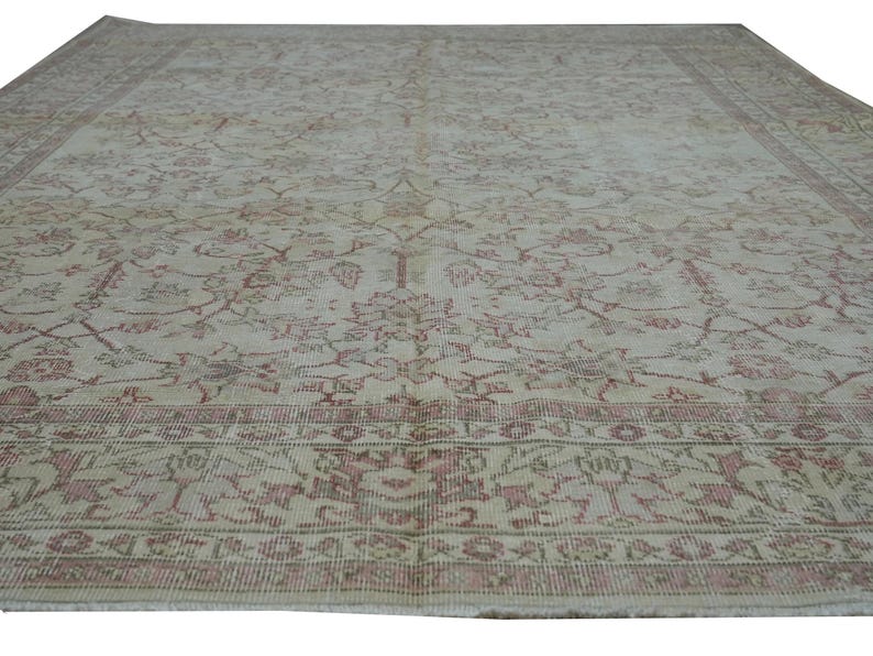 May include: A large, rectangular rug with an intricate floral pattern in shades of beige and faded rose. The rug features a detailed border and a distressed, vintage appearance, suitable for home decor.