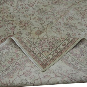 May include: A vintage area rug with a floral pattern in shades of beige, cream, and faded red. The rug's corner is folded up, revealing a detailed border design. The overall aesthetic is antique and well-worn.