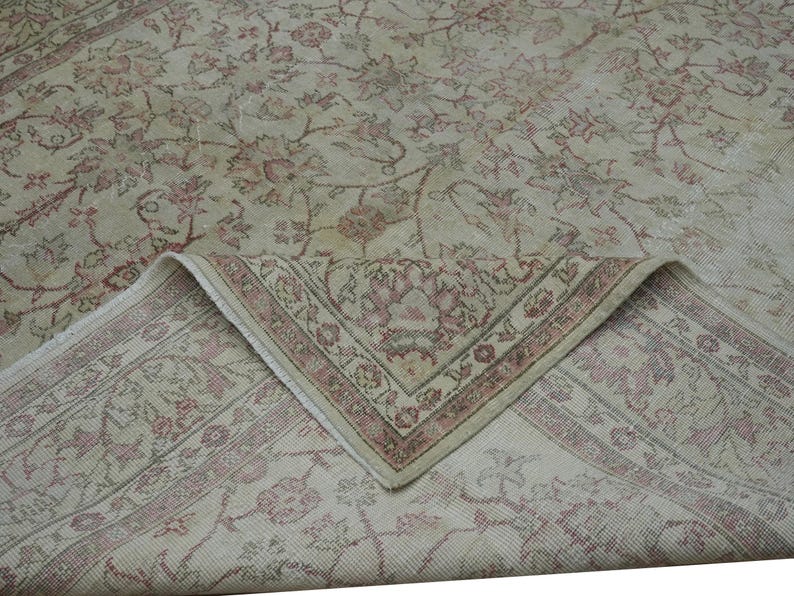 May include: A vintage area rug with a floral pattern in shades of beige, cream, and faded red. The rug's corner is folded up, revealing a detailed border design. The overall aesthetic is antique and well-worn.