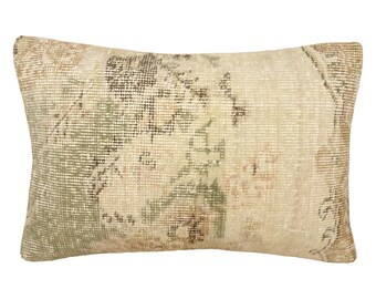 Puede incluir: Un cojín rectangular con un patrón textil tejido en tonos apagados de beige, verde salvia y marrón descolorido. El diseño muestra una apariencia desgastada y envejecida con intrincados motivos geométricos y florales en toda la superficie.