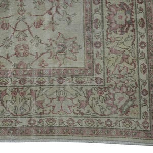 May include: A section of a vintage rug with a faded floral pattern in shades of beige, pink, and muted green. The rug features a detailed border and a distressed appearance, suggesting age and use. The design is symmetrical and ornate.