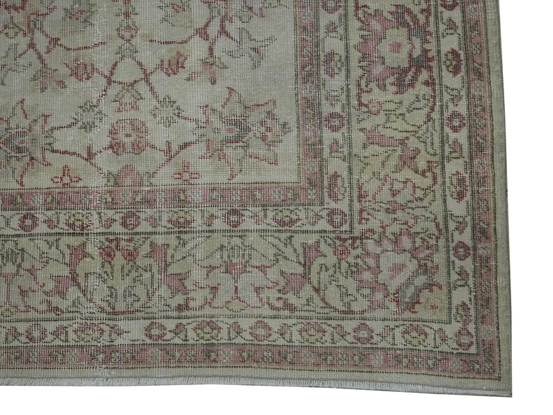 May include: A section of a vintage rug with a faded floral pattern in shades of beige, pink, and muted green. The rug features a detailed border and a distressed appearance, suggesting age and use. The design is symmetrical and ornate.