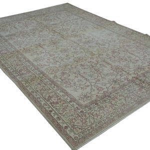 May include: A large, rectangular rug with an intricate floral pattern in shades of cream, beige, and muted red. The rug features a detailed border and a distressed, vintage appearance, suitable for living rooms or bedrooms.