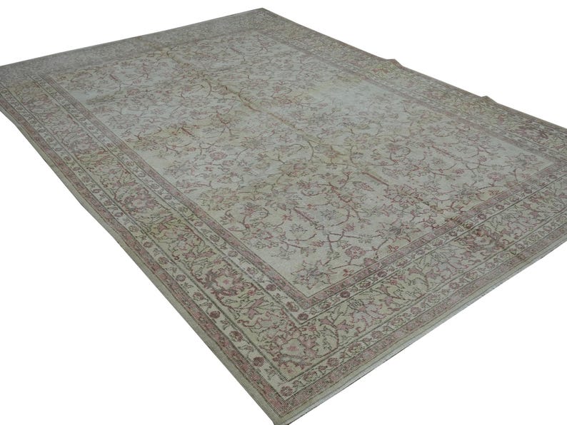 May include: A large, rectangular rug with an intricate floral pattern in shades of cream, beige, and muted red. The rug features a detailed border and a distressed, vintage appearance, suitable for living rooms or bedrooms.