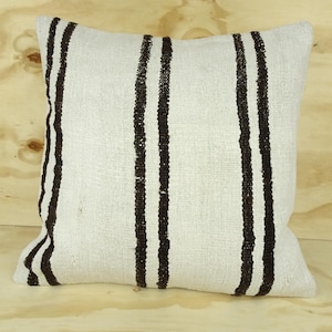 Może przedstawiać: Biała poduszka w czarne paski. Poduszka jest wykonana z miękkiej, tkanej tkaniny.