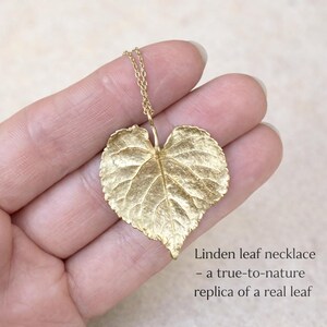 Puede incluir: Un collar de hoja de tilo dorado con una cadena delicada. El colgante es una r&eacute;plica detallada de una hoja real, que muestra vetas y textura intrincadas. El texto de la imagen dice: "Linden leaf necklace - a true-to-nature replica of a real leaf."