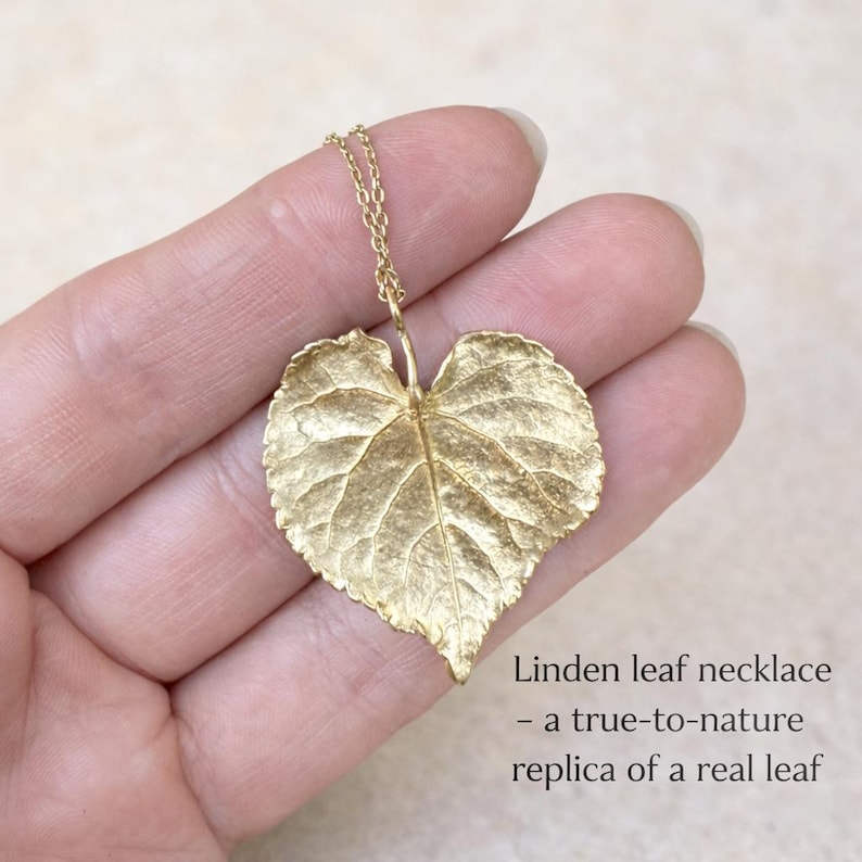 Puede incluir: Un collar de hoja de tilo dorado con una cadena delicada. El colgante es una r&eacute;plica detallada de una hoja real, que muestra vetas y textura intrincadas. El texto de la imagen dice: "Linden leaf necklace - a true-to-nature replica of a real leaf."