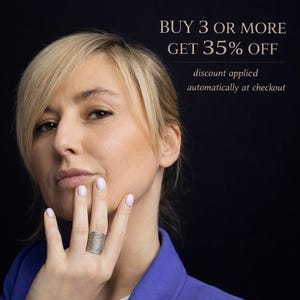 May include: A woman wearing a silver ring with an intricate design. The ring is on the ring finger of her left hand. The image includes text that reads "BUY 3 OR MORE GET 35% OFF" and "discount applied automatically at checkout."