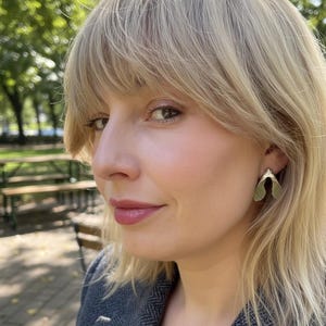 May include: A silver-toned earring shaped like a maple seed pod, also known as a samara, featuring a smooth, metallic finish. The earring is worn on the earlobe and has a distinct bifurcated design that mimics the natural form of a winged seed.