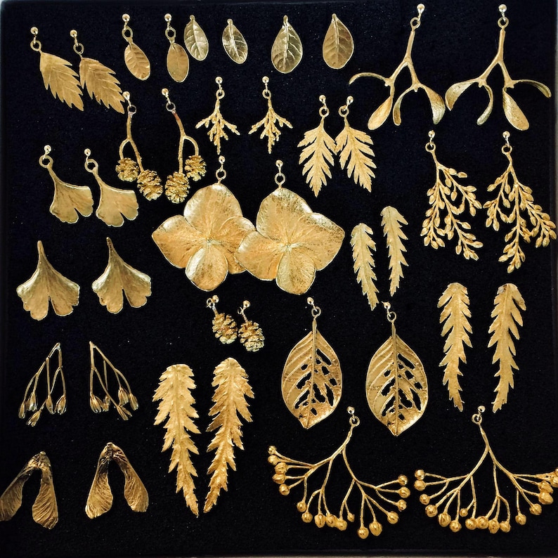 Puede incluir: Una colecci&oacute;n de pendientes dorados con diversos dise&ntilde;os bot&aacute;nicos, incluyendo hojas, ramas y formas de flores. Los pendientes se exhiben sobre una superficie negra, mostrando sus intrincados detalles y variados estilos. La colecci&oacute;n incluye varios pares de pendientes.
