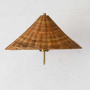 May include: A woven wicker lampshade with a conical shape hangs from a ceiling fixture. The lampshade is a light brown colour and has a simple, elegant design.