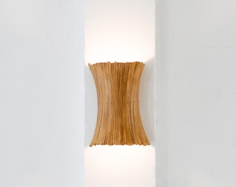 May include: A wooden wall sconce with a light brown finish. The sconce has a cylindrical shape and is made of thin, vertical slats.