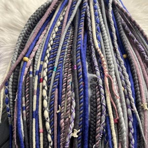 a close-up view of a variety of braided hair accessories in different colors and patterns, including shades of blue, gray, purple, and white.