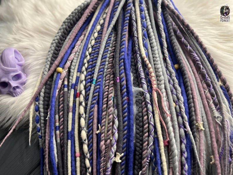a close-up view of a variety of braided hair accessories in different colors and patterns, including shades of blue, gray, purple, and white.
