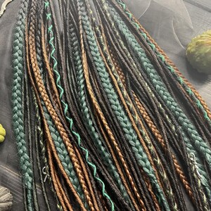 a variety of braided hairstyles, including braids in different colors and styles, arranged on a wooden surface. There are also some small objects, such as a pumpkin and a pair of scissors, placed alongside the braids.