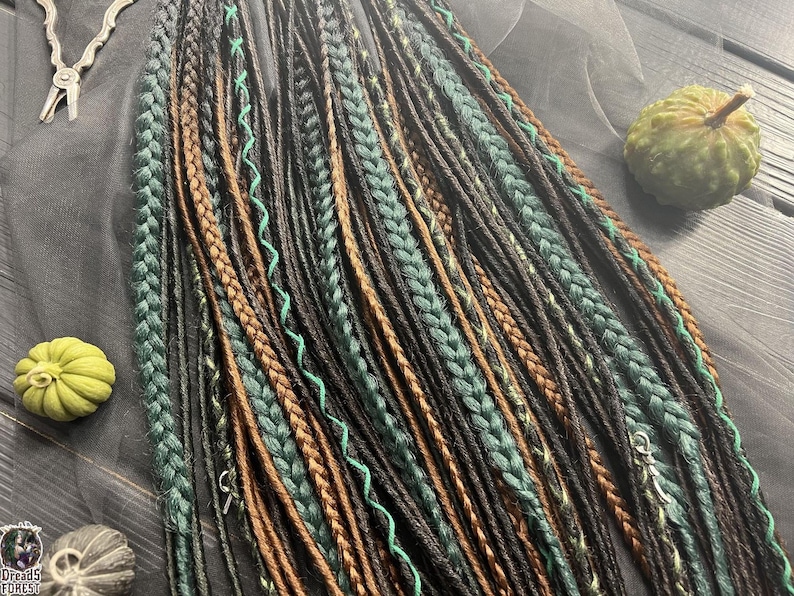 a variety of braided hairstyles, including braids in different colors and styles, arranged on a wooden surface. There are also some small objects, such as a pumpkin and a pair of scissors, placed alongside the braids.