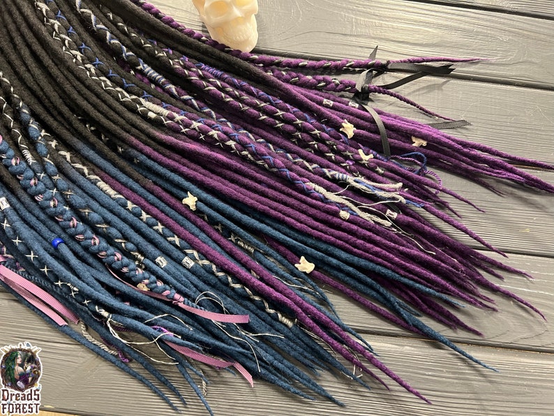 Puede incluir: Un conjunto de rastas sint&eacute;ticas en tonos negro, azul oscuro y morado. Las rastas est&aacute;n decoradas con bordados blancos y azules y tienen una variedad de texturas.