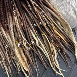 May include: A set of brown and white synthetic dreadlocks with brown leather and beads. The dreadlocks are tied together with a brown leather cord.