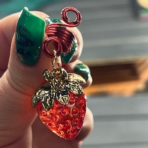A hand holding a decorative strawberry charm with a red spiral design.